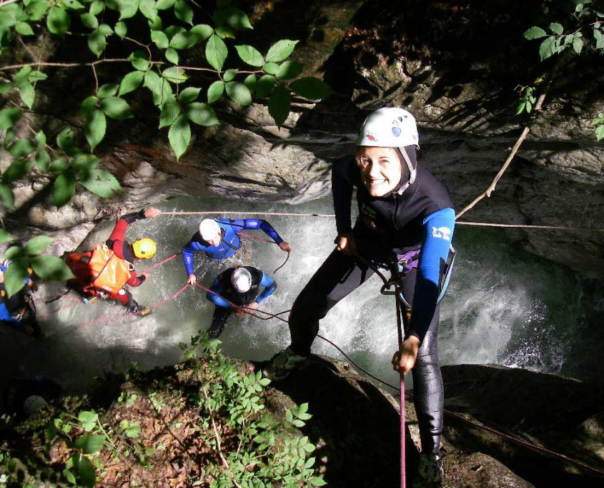 Canyoning-Teilnehmerin beim Abseilen über einer Gruppe in einer Schlucht