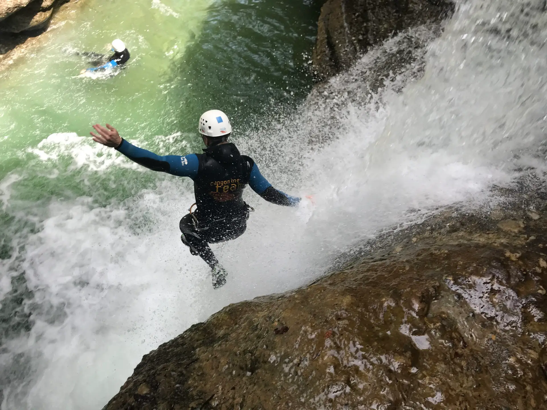 Person beim Canyoning-Sprung neben einem Wasserfall